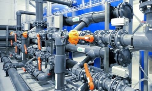 Large industrial water treatment and boiler room. Shiny steel metal pipes and blue pumps and valves.
